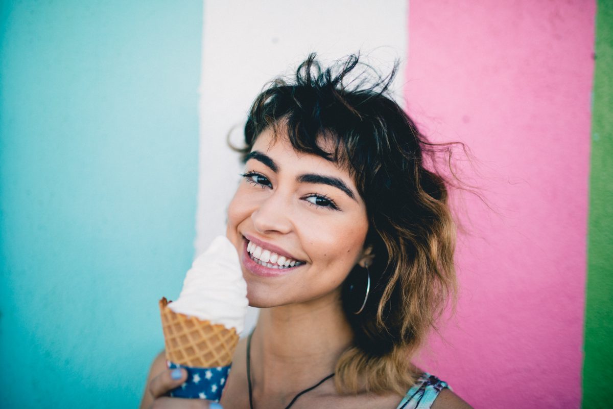 A smiling woman in front of a colorful, striped background, holding an ice cream cone.